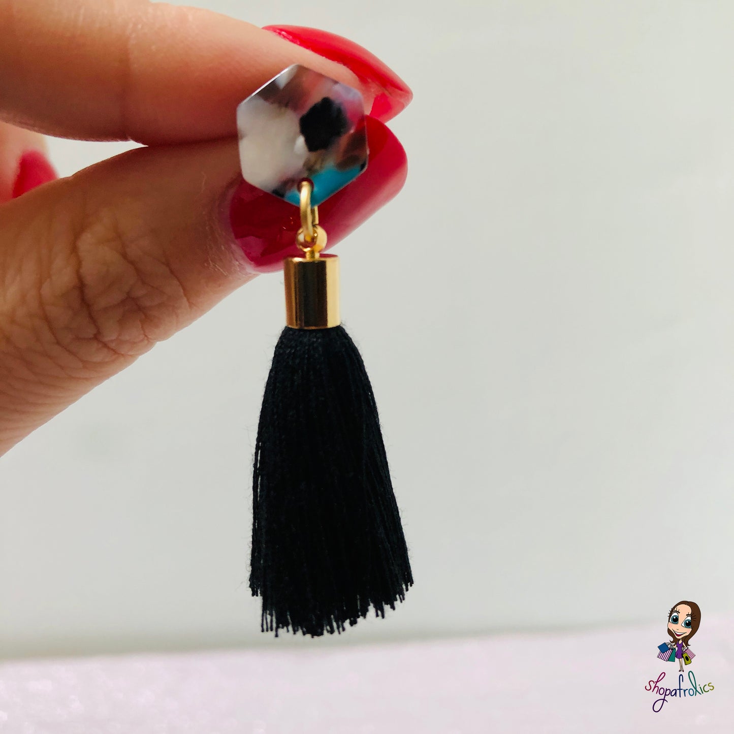 Close up of one black cotton tassel drop earrings are finished with a vibrant coloured hexagon acrylic ear stud. 