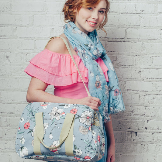 A versatile canvas weekend bag in vibrant delicate floral design print, on a solid blue coloured background. A mini break essential!